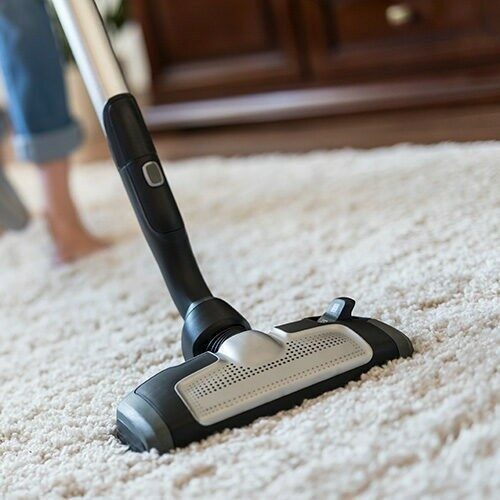 Young woman using a vacuum cleaner while cleaning carpet in the house.